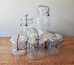 mason jars with lids are sitting on a wooden table next to some other glass jars