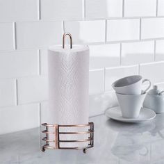 a white toilet paper holder sitting on top of a counter next to a cup and saucer