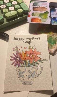 a mother's day card with flowers in a teacup on a table next to a calculator