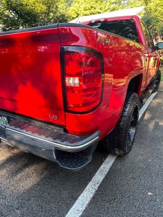 the rear end of a red truck parked in a parking lot with trees behind it