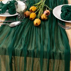 a table topped with plates and napkins covered in green cloth next to tulips