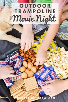 kids and their dog are playing with the movie night snacks on a tray that is full of popcorn