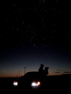 two people are sitting on the hood of a car at night with stars in the sky