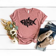 Looking for a funny shark shirt? Check out our selection of shark shirts! Our cute shark shirt is perfect for babies and toddlers. Or give the gift of sharks with our great white shark shirt or shark family shirt. Whatever your favorite shark, we've got it! Our  T-shirts are High Quality, SUPER soft and SUPER comfy. They made of 100% Cotton.  T-Shirt Brands and Model *Unisex T-shirts are Bella Canvas 3001 *Unisex V-Neck Tees are Bella Canvas 3005  *Women Tank Tops are Next Level  *Youth T-Shirts Shark Shirts Vinyl, Shark Week Outfit, I Love Shark Shirts, Shark Week Shirts, Shark Shirt Ideas, Casual Short Sleeve Shark Design Tops, Casual Short Sleeve T-shirt With Shark Design, Casual Cotton T-shirt With Shark Design, Casual Short Sleeve Top With Shark Design