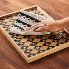 a person is using a cloth to clean a wooden tray with black and white designs on it