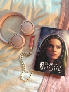 a book, headphones, and necklace laying on a bed with a pink blanket