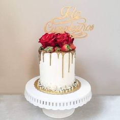 a white cake topped with red roses on top of a white cake plate and gold lettering