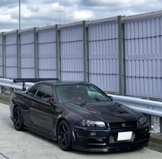 a black car parked on the side of a road next to a wall with windows