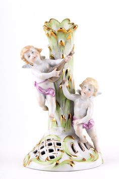 two figurines sitting on top of a green and white plant with gold trimmings