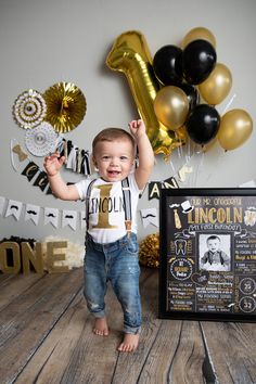 a baby boy is standing in front of balloons and a sign with the number one on it