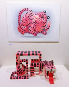 a pink and black animal sitting on top of a white table next to a painting