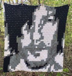 a black and white quilt hanging on a wire fence with trees in the back ground