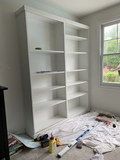 an empty room with white bookcases and construction tools on the floor next to it