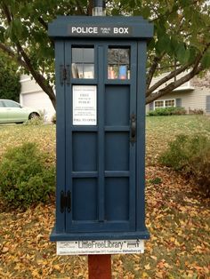 a blue police box sitting on top of a wooden pole next to a leaf covered yard