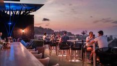 people are sitting at tables on the roof of a building with blue lights in the background