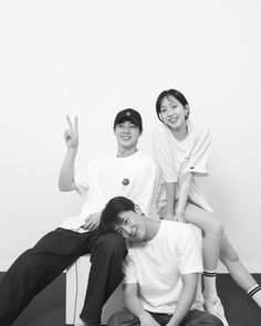 three people sitting on top of each other in front of a white wall with one person giving the peace sign