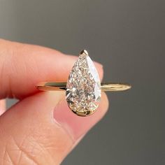 a woman's hand holding a yellow gold engagement ring with a pear shaped diamond