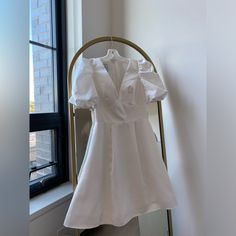 a white dress hanging on a rack in front of a window with a brick wall