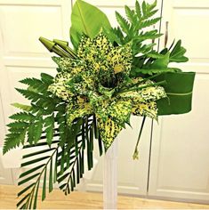 a vase filled with lots of green plants on top of a wooden table next to a white door