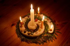 a cake with lit candles on it sitting on top of a wooden table next to pine branches