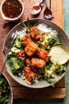 a bowl filled with chicken and rice on top of a wooden table next to bowls of sauce