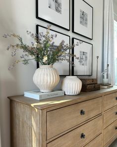 two white vases sitting on top of a wooden dresser next to pictures and flowers