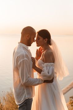 a man and woman standing next to each other in front of the ocean at sunset