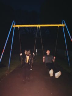 two children playing on swings at night in the park, one is swinging and the other is sitting down