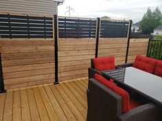 a wooden deck with chairs and table next to a fenced in area that looks like it has been built into the side of a house