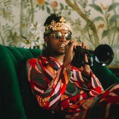 a man sitting on top of a green couch holding a trumpet in his hand and wearing a crown