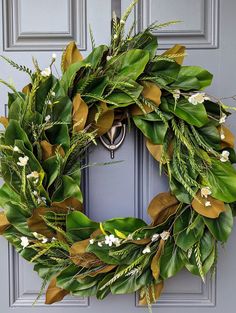 a green wreath with white flowers and greenery hangs on the front door of a house