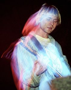 a man with long hair playing a guitar in front of a microphone and some lights