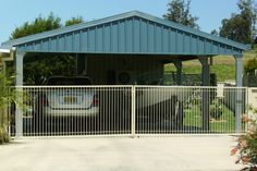 a car is parked in front of a metal fenced driveway area with a carport