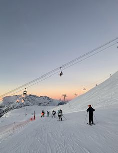 skiers and snowboarders at the bottom of a ski slope as the sun sets