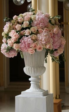 a white vase filled with pink flowers sitting on top of a table next to a sign