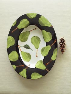 a black and white plate with green leaves on it next to a pinecone