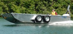 a man riding on the back of a silver boat in a body of water with trees behind him