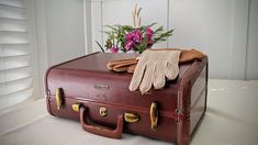 an old suitcase with gloves and flowers in the background