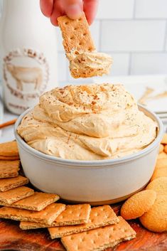 a person dipping crackers into a bowl of hummus with crackers around it