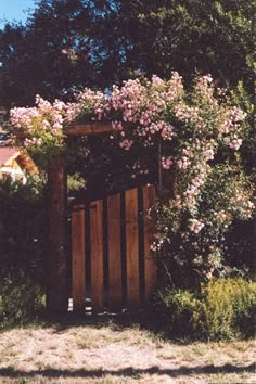 an open wooden gate with pink flowers growing over it