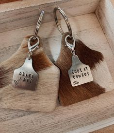 two cow hide keychains that say drive safe and cool it cowboy