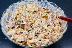 a glass bowl filled with pasta salad on top of a blue countertop next to a red spoon