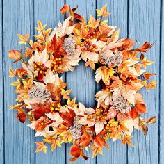 a wreath with autumn leaves and berries hanging on a blue wooden door, ready to be used as a decoration