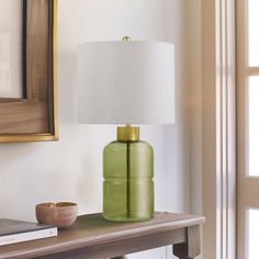 a green lamp sitting on top of a wooden table next to a book and a painting