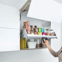 a woman holding a tray with food on it in a kitchen cabinet under an overhead light