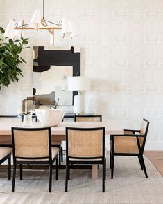 a dining room table and chairs in front of a wall with abstract art on it