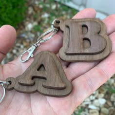 two wooden key chains in the palm of someone's hand, with letters carved into them