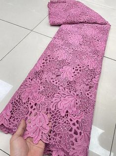 a person is pointing at a pink lace fabric on the floor with white tiles in the background