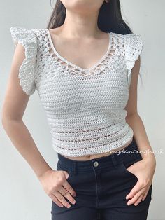 a woman with her hands on her hips wearing a white crochet top and black jeans