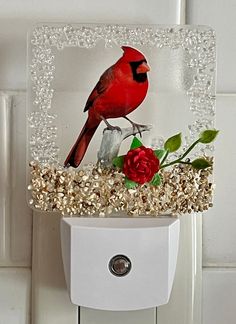 a red bird sitting on top of a glass block with flowers in front of it